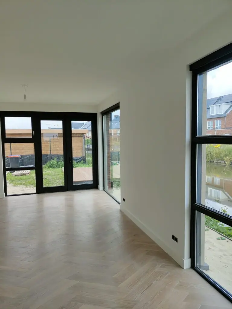 Moderne woning met visgraadvloer en antraciete kozijnen. De wanden en plafonds zijn glad gestuct en ze hebben latex laten spuiten voor een strakke afwerking.