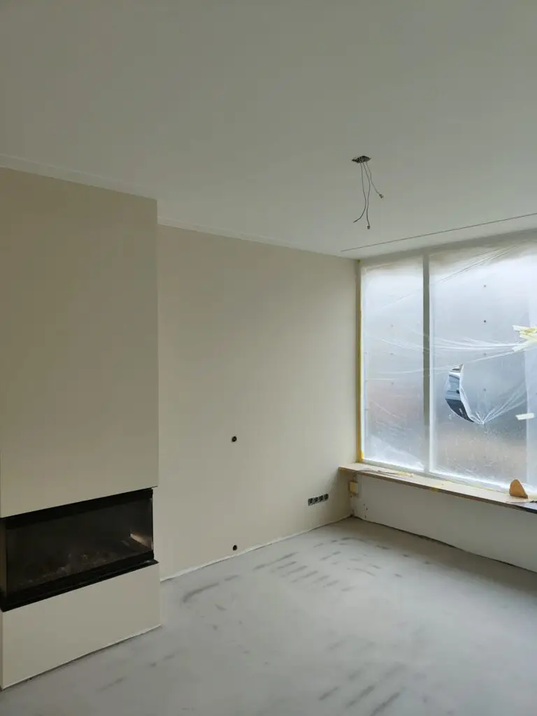 Moderne woonkamer in aanbouw met ingebouwde open haard, grote raam met afdekfolie en onafgewerkte vloeren.