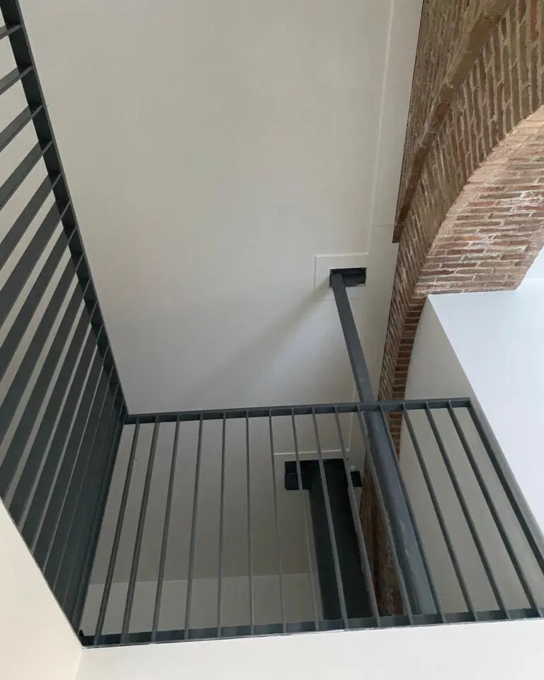 Zicht op vide van een tot woning omgebouwde kerk. De railing van de vide is afgewerkt in zwart metaal. De oude kerkboog uit baksteen is nog zichtbaar. Dit steekt af tegen de glad gestucte plafonds en wanden die in het wit afgewerkt zijn met latex.